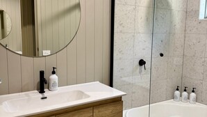 Et moderne badeværelse med en hvid vask, trækommode, et stort spejl og en brusekabine i glas.