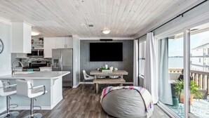 Une cuisine moderne avec des meubles blancs, un îlot central doté de tabourets, une table à manger avec des chaises et une grande fenêtre offrant une vue sur la mer.