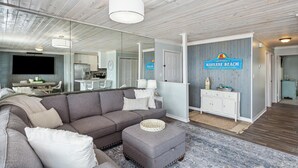 Un salon moderne avec un canapé d’angle gris, un petit pouf et un tapis à motifs bleus.