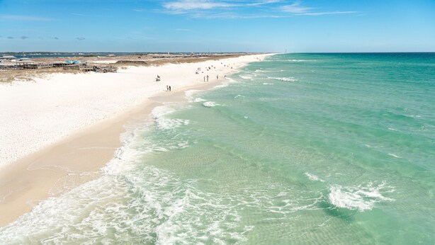 Une plage avec une eau turquoise et limpide, un rivage sablonneux et une jetée.