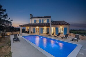 A two-story house with a swimming pool, outdoor seating, and a view of the countryside.