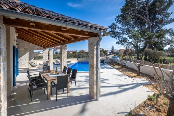 A covered outdoor patio with a pool, stone pillars, and outdoor furniture.