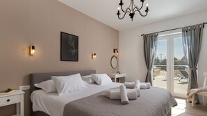 A hotel room with a large bed, bedside tables, a desk, a chandelier, a window with curtains, and a view of the outside. - Villa Mediterra Prima Zadarvillas (Nin)