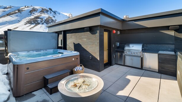 Een moderne buitenkeuken met een barbecue en een jacuzzi, met op de achtergrond een besneeuwde berg.