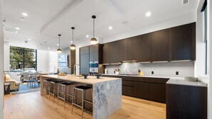 Een moderne keuken met een marmeren eiland, donkere houten kastjes en hanglampen.