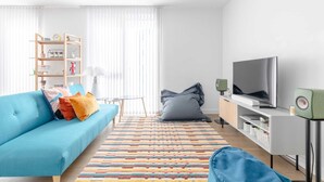 A modern living room with a blue sofa, a colorful striped rug, a television, and a bookshelf. - Stylish 2BD Oasis W/balcony South East London! (London)