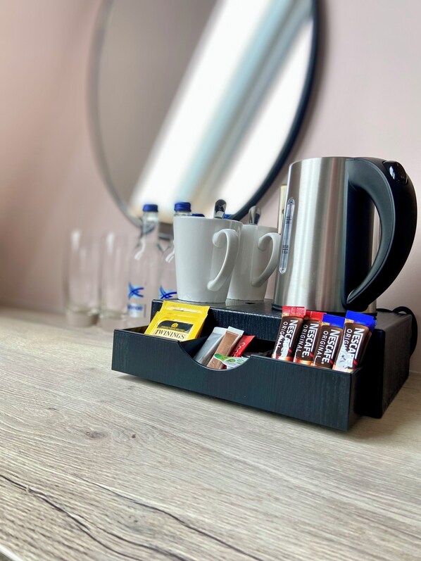A coffee maker, two white mugs, and a coffee pod holder with Nescafe and Twinings coffee pods on a wooden surface.