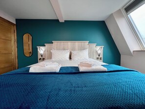 A neatly made bed with white linens and a blue blanket, a wooden headboard, and a teal accent wall. - The Bath Rooms (Morecambe)