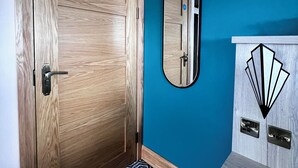 A room with a wooden door, a mirror, and a blue wall. - The Bath Rooms (Morecambe)