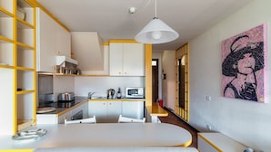 Cocina compacta con armarios blancos, microondas y estufa. Hay un comedor con mesa y sillas blancas.