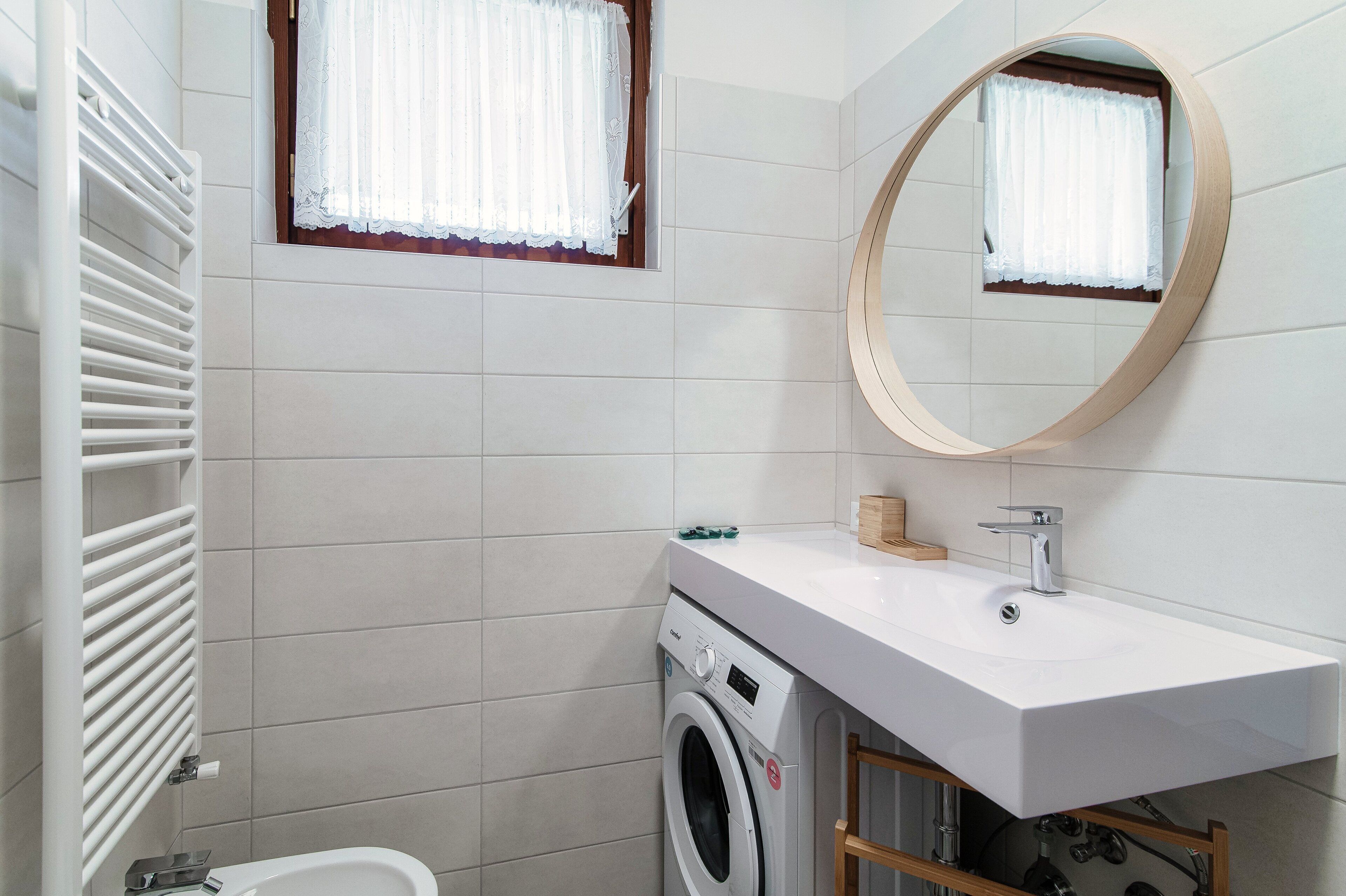 Ein modernes Badezimmer mit Waschmaschine, Waschbecken mit Spiegel und einem Fenster mit Vorhängen.