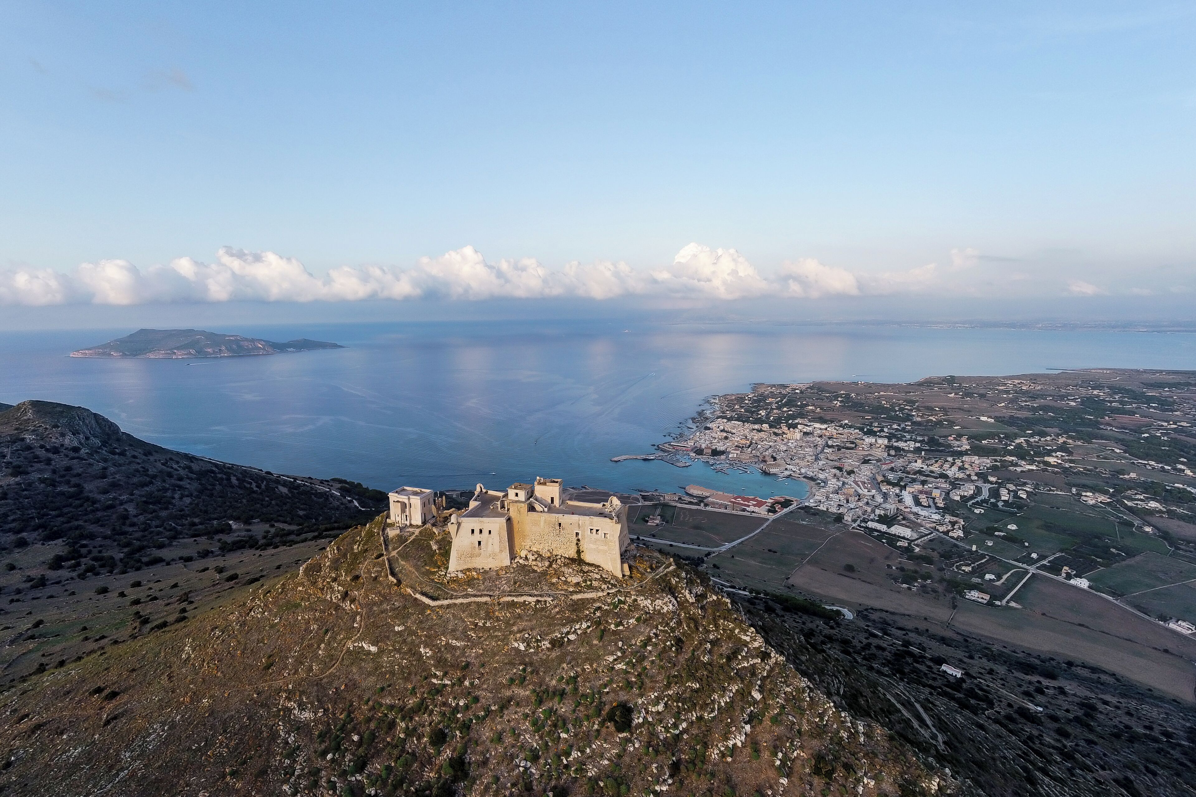 Una cittadina costiera con un castello imponente su una collina, circondata da campi e da un corso d'acqua.