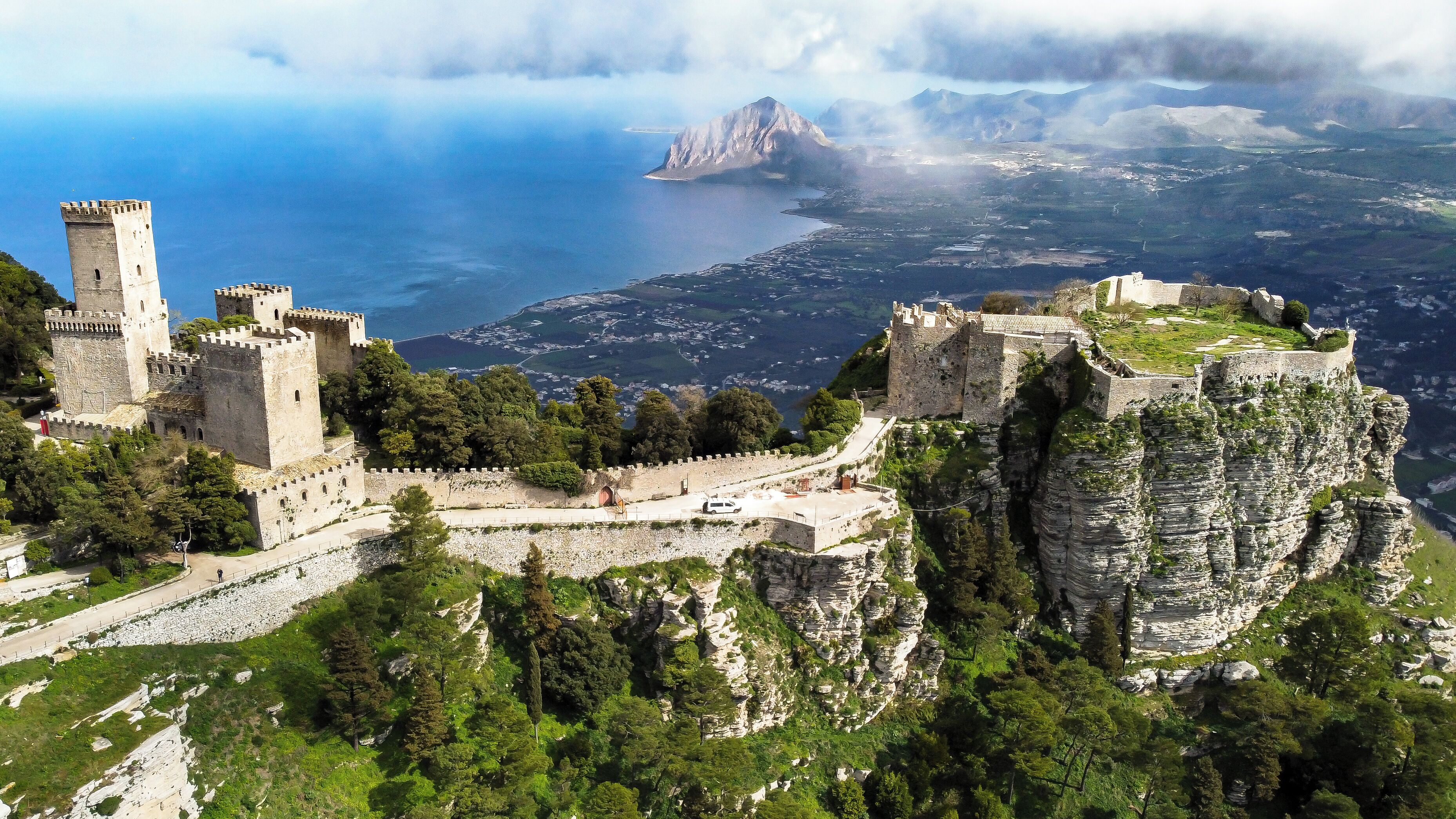 A historic castle with a fortified wall, a tower, and a scenic view of a coastal landscape.