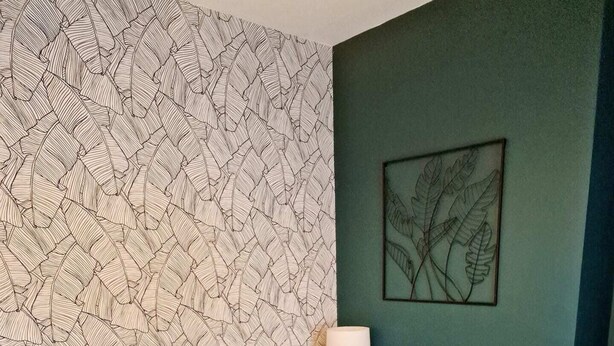 A neatly made bed with a dark blanket, a wall with a leaf pattern, and a framed plant on the wall. - Fantastic Home! Football Fans -5 min to Stadium (Liverpool)
