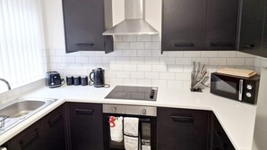 A modern kitchen with dark cabinets, a stainless steel range hood, a microwave, a toaster, and a kettle. - Fantastic Home! Football Fans -5 min to Stadium (Liverpool)