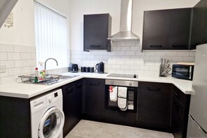 A compact kitchen with a washing machine, a sink, a microwave, and dark cabinets. - Fantastic Home! Football Fans -5 min to Stadium (Liverpool)