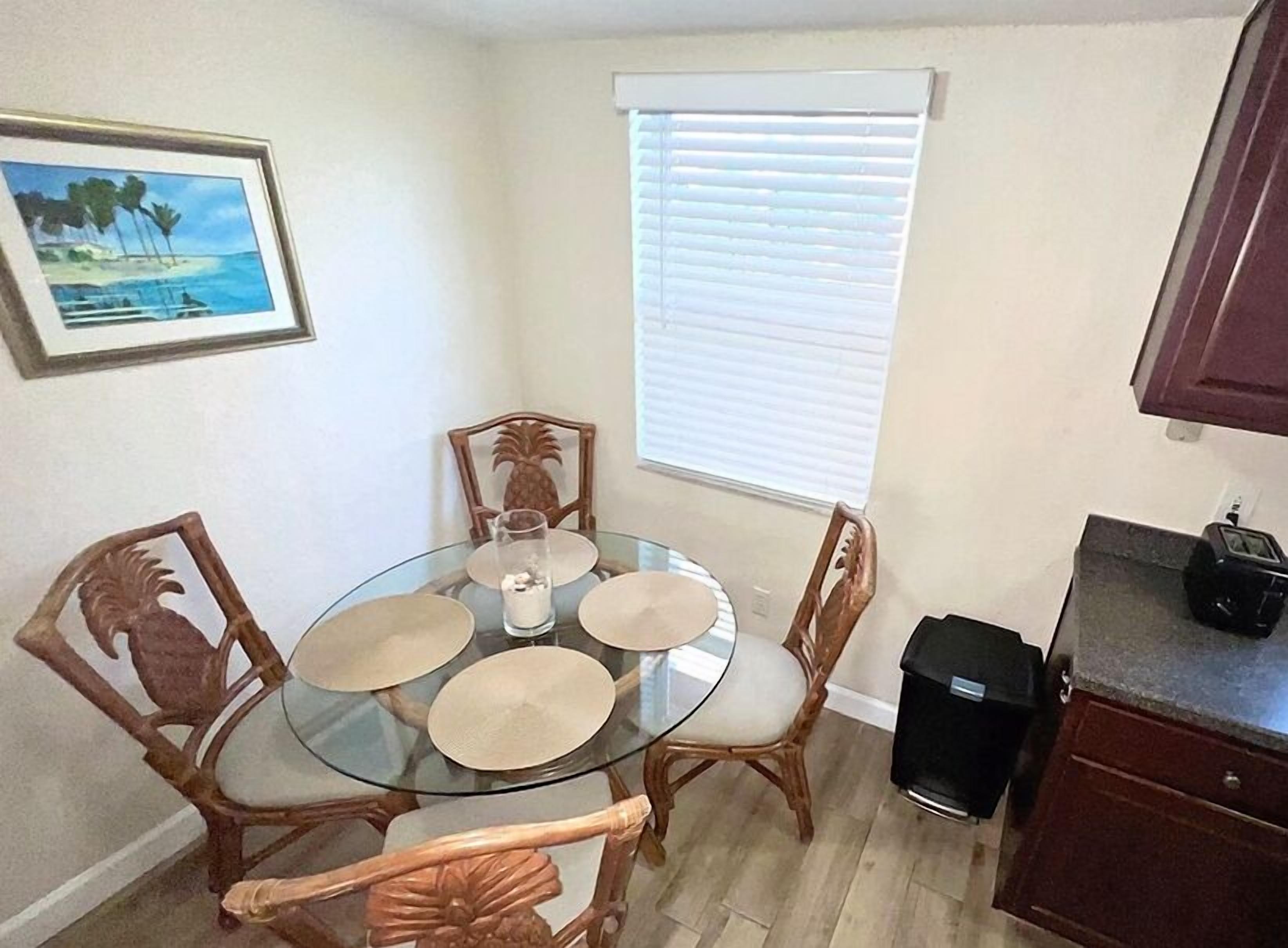 A dining area with a glass table, four chairs, and a window with blinds.