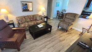 A living room with a sofa, armchair, coffee table, and a TV mounted on the wall. - Coral Shores Resort (North Redington Beach)