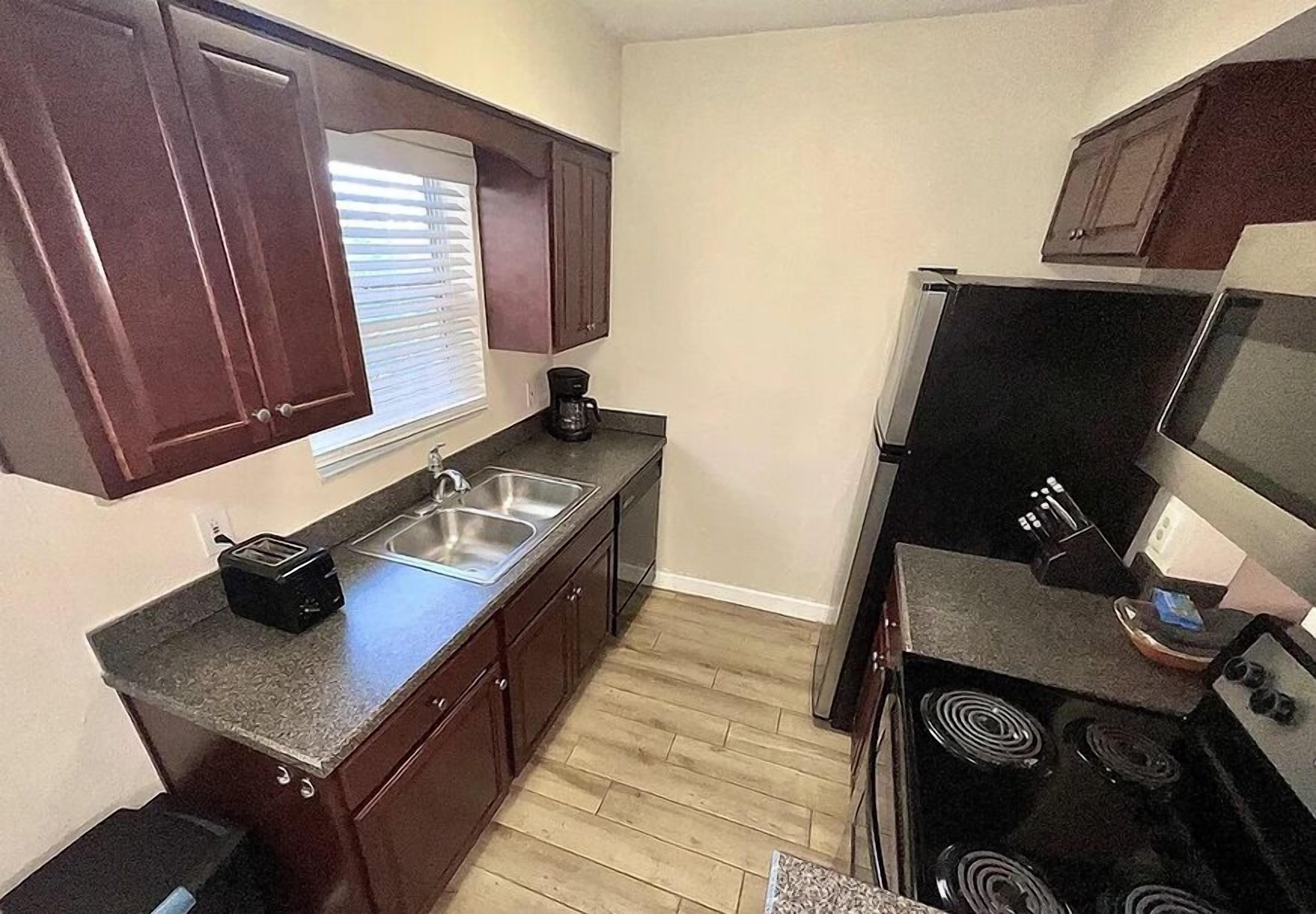 Cocina compacta con armarios de madera oscura, horno empotrado y cafetera.