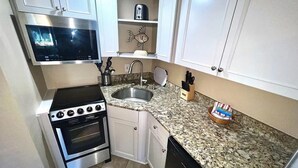 A compact kitchen with white cabinets, a stainless steel stove, a sink, and a granite countertop. - Coral Shores Resort (North Redington Beach)