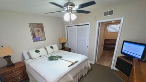 A bedroom with a bed, nightstands, a ceiling fan, a TV, and a door leading to another room. - Coral Shores Resort (North Redington Beach)