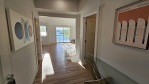 A hallway with wooden flooring, a glass railing, and a framed picture on the wall.
