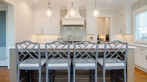 Una cocina moderna con armarios blancos, un salpicadero de baldosas tipo espiga y una isla central con taburetes de bar.