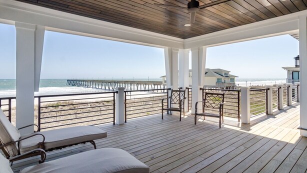Una terraza cubierta al aire libre con suelo de madera, barandas blancas y vistas a la playa y al océano.