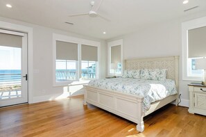Quarto com cama grande, ventoinha no teto e vista para o oceano pelas janelas.