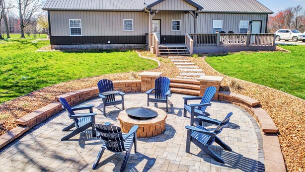 Eine Terrasse mit Adirondack-Stühlen und einer runden Feuerstelle.