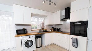 A modern kitchen with white cabinets, a built-in washing machine, a stainless steel trash bin, and a black oven. - 5 Guests - 2-bed House - Bbq - Free Parking (Norwich)