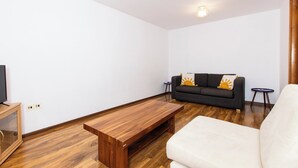 A modern living room with a wooden coffee table, a sofa with cushions, and a television on a wooden cabinet. - 5 Guests - 2-bed House - Bbq - Free Parking (Norwich)