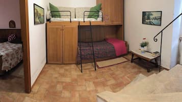 A room with a bunk bed, a wooden wardrobe, a small table with a plant, a staircase, and a painting on the wall.