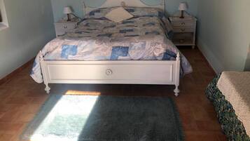 Un dormitorio con una cama, dos mesitas de noche, una mesita auxiliar, una alfombra y un cuadro enmarcado en la pared.
