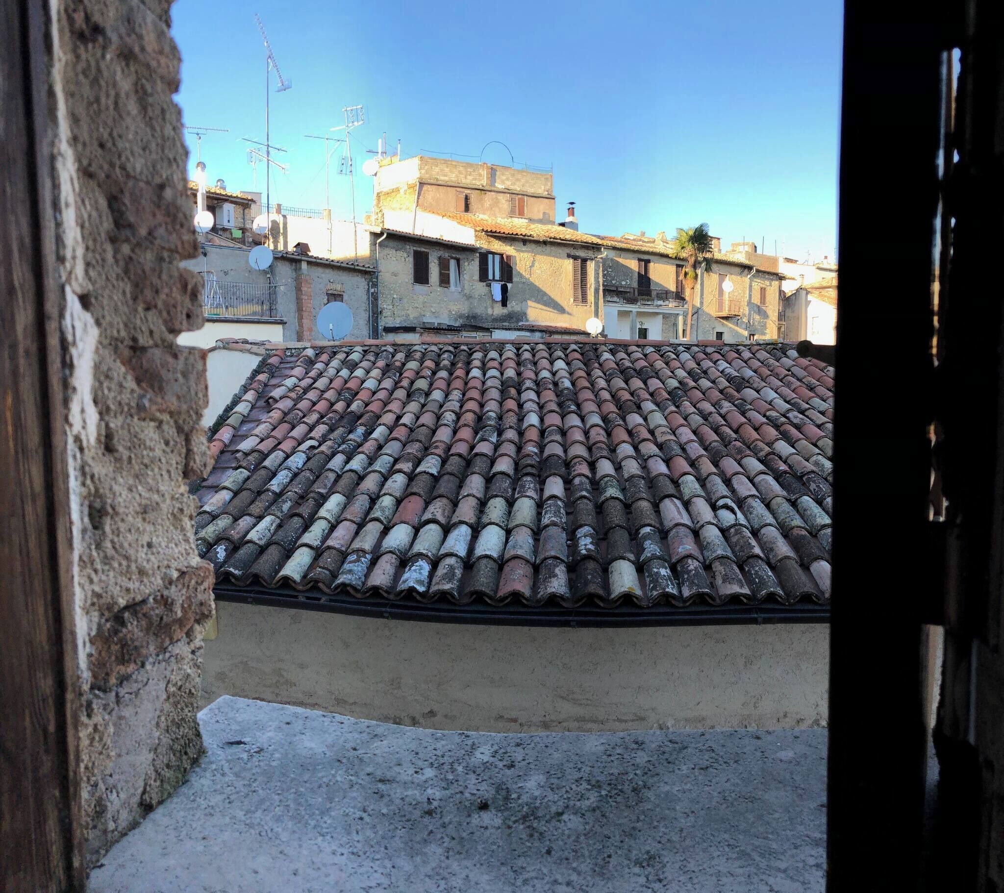 Terraço com telhas de terracota antigas, céu claro e edifícios ao redor.