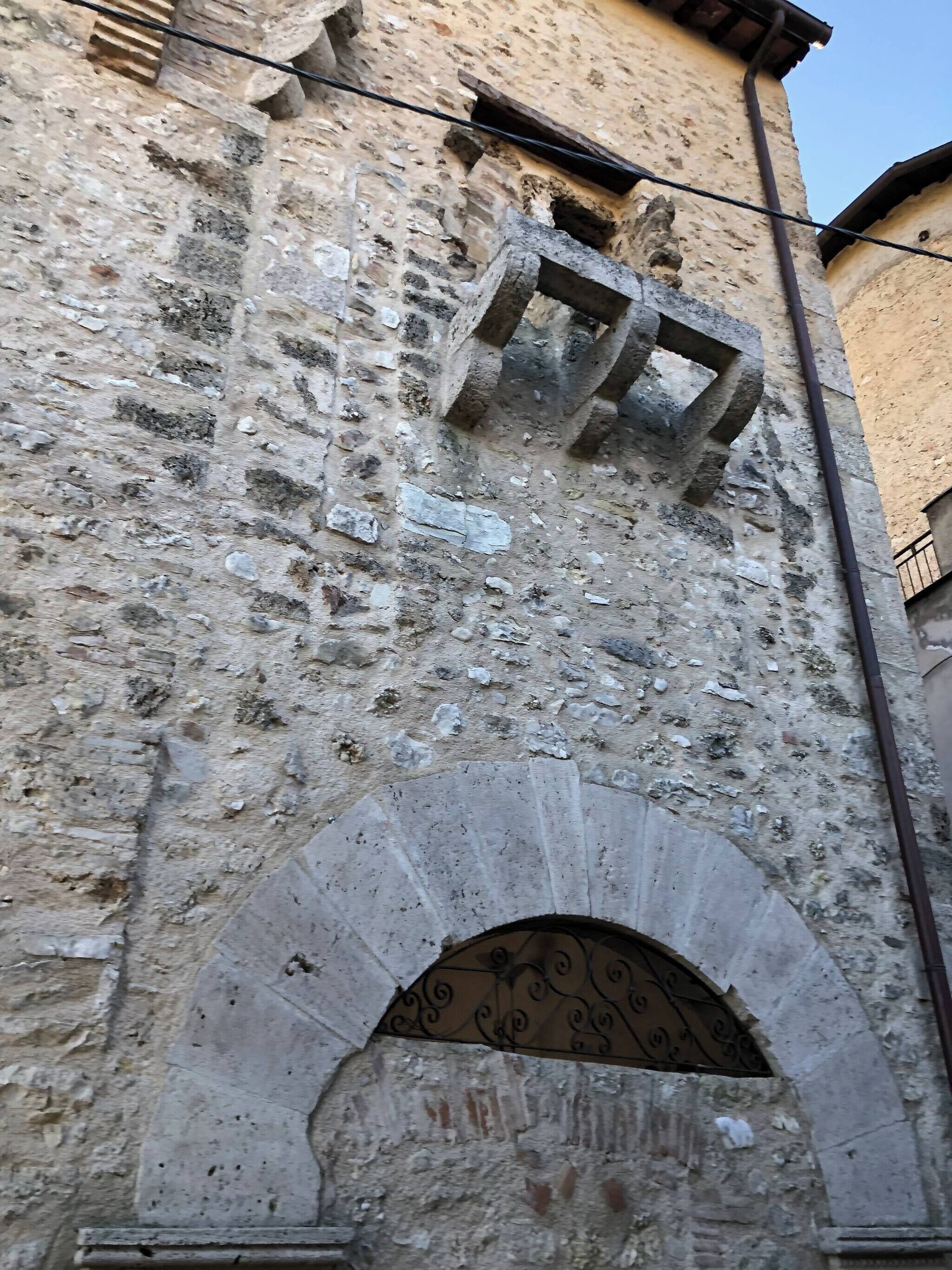 En byggnad av sten med en fasad som vittrat med tiden, en balkong av metall och en välvd dörröppning.