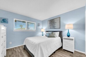A bedroom with a bed, two bedside tables with lamps, a dresser, a window with blinds, and artwork on the walls. - 🌟 50Ft from Beach Access- Pool View- Budget Friendly- 1BR Nautical Watch E-3🌟 (Panama City Beach)