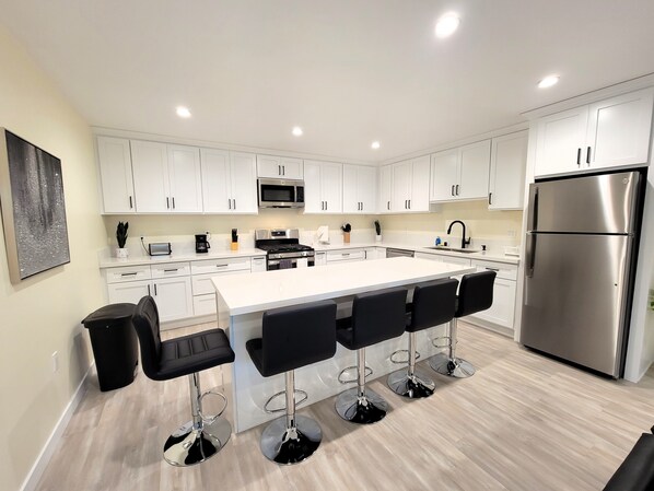 A modern kitchen with white cabinets, a stainless steel refrigerator, and a central island with bar stools.