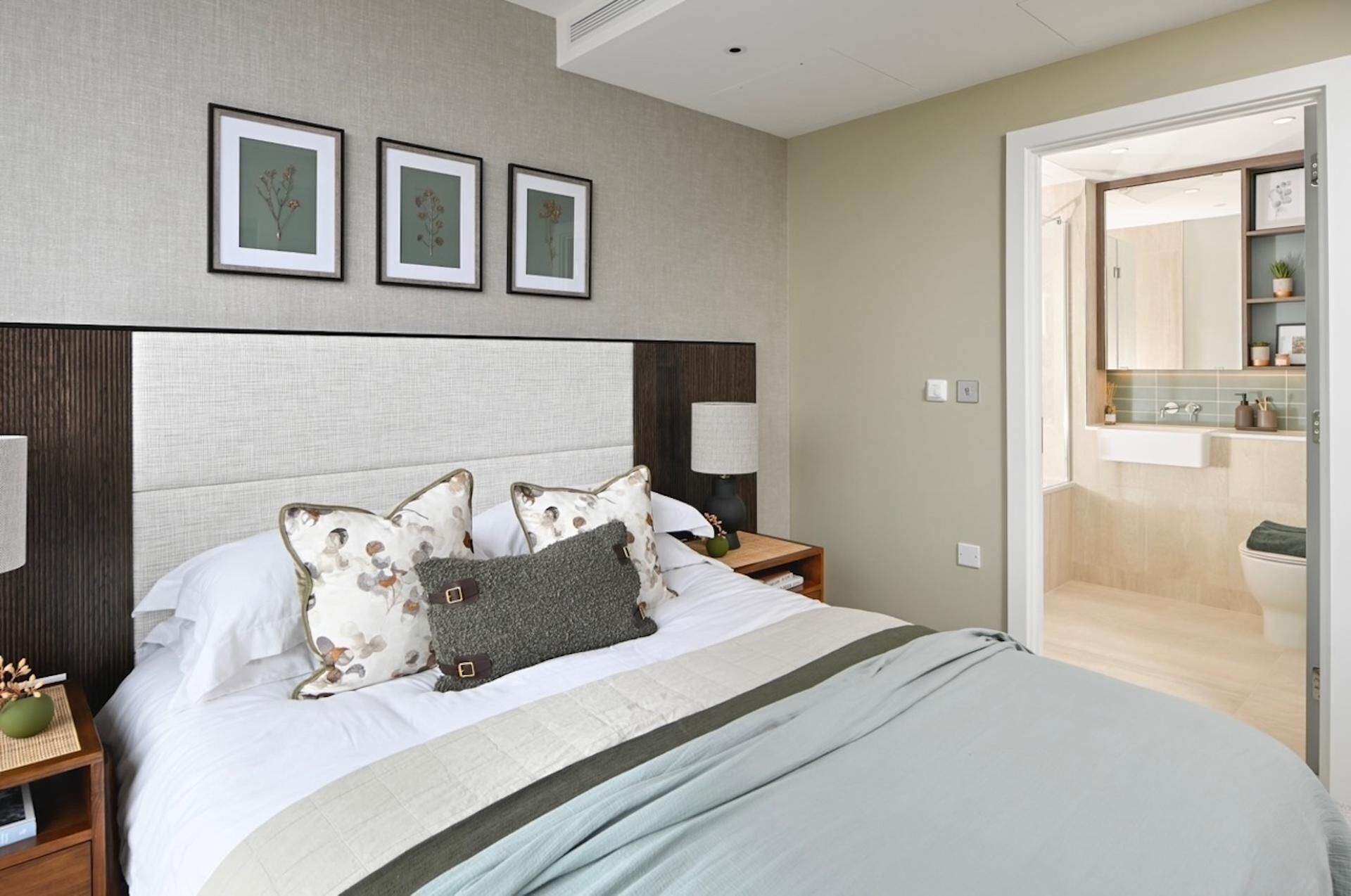 A modern hotel room with a large bed, a nightstand with a lamp, and a bathroom visible through an open door.