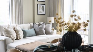A modern living room with a sofa, dining table, and a vase of dried flowers. - Designer Penthouse Panoramic Views London 2 Beds (London)