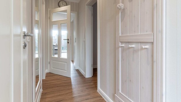 A hallway with wooden flooring, white walls, and a door leading to a room with a view. - Ferienwohnung in Westerdeichstrich (Westerdeichstrich)