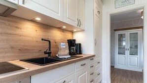A modern kitchen with white cabinets, a wooden countertop, a built-in stove, and a coffee maker. - Ferienwohnung in Westerdeichstrich (Westerdeichstrich)