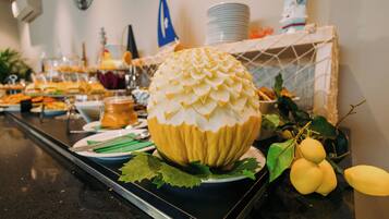 A buffet table with a large decorative fruit centerpiece, plates, and various food items.