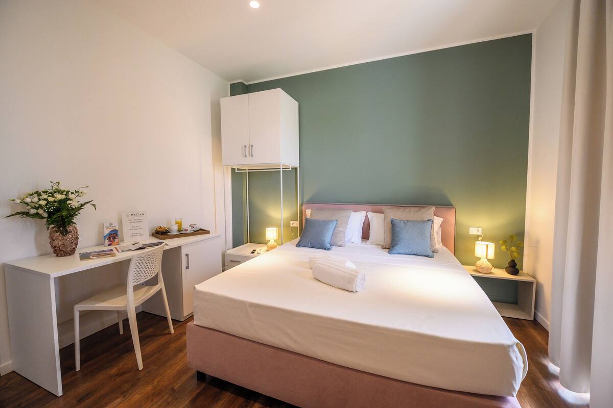 A neatly arranged hotel room with a bed, a desk, a chair, and a small table with a plant.