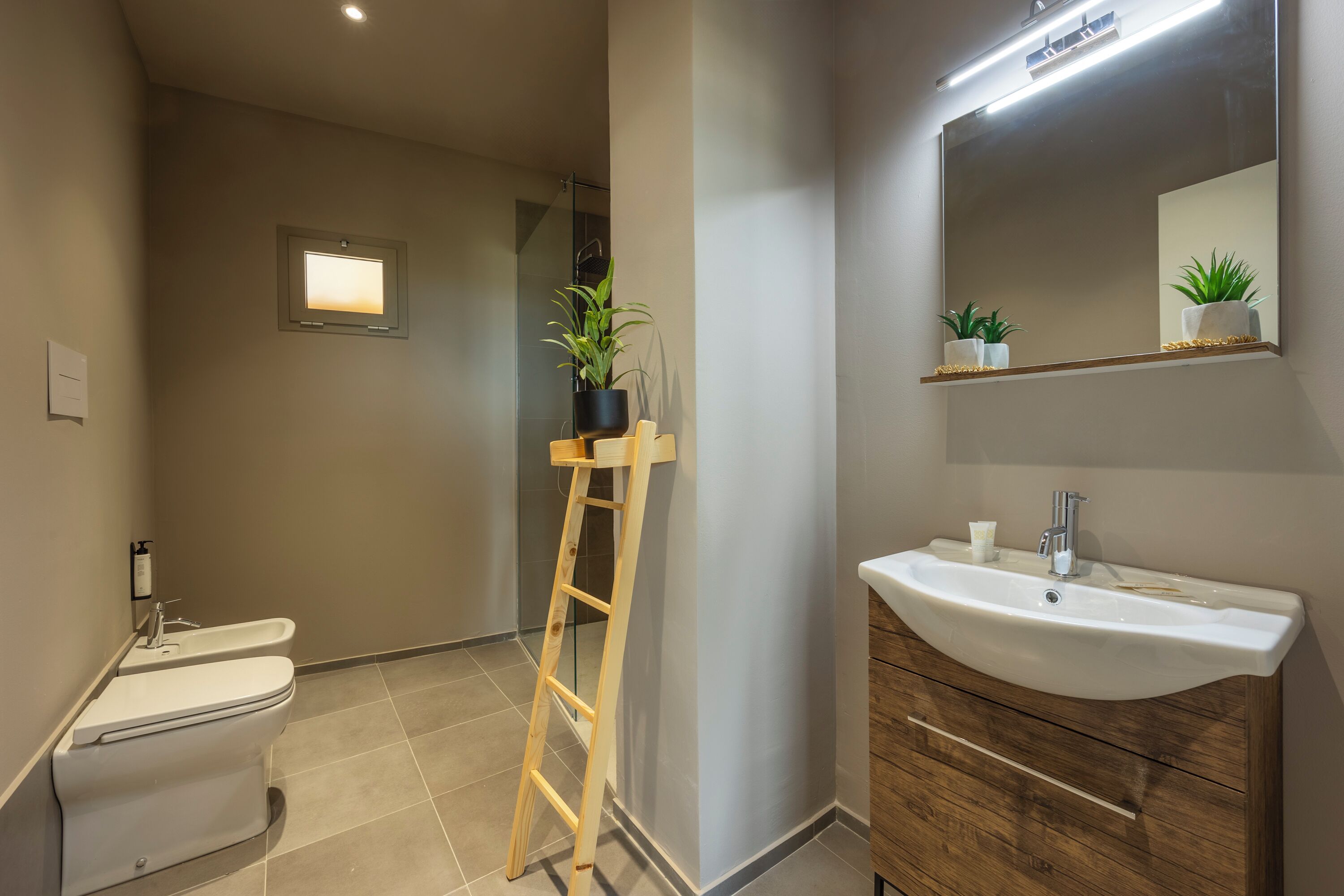 Un baño con inodoro, bidé, tocador de madera con lavabo y un espejo.