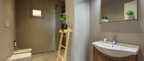 Un baño con inodoro, bidé, tocador de madera con lavabo y un espejo.