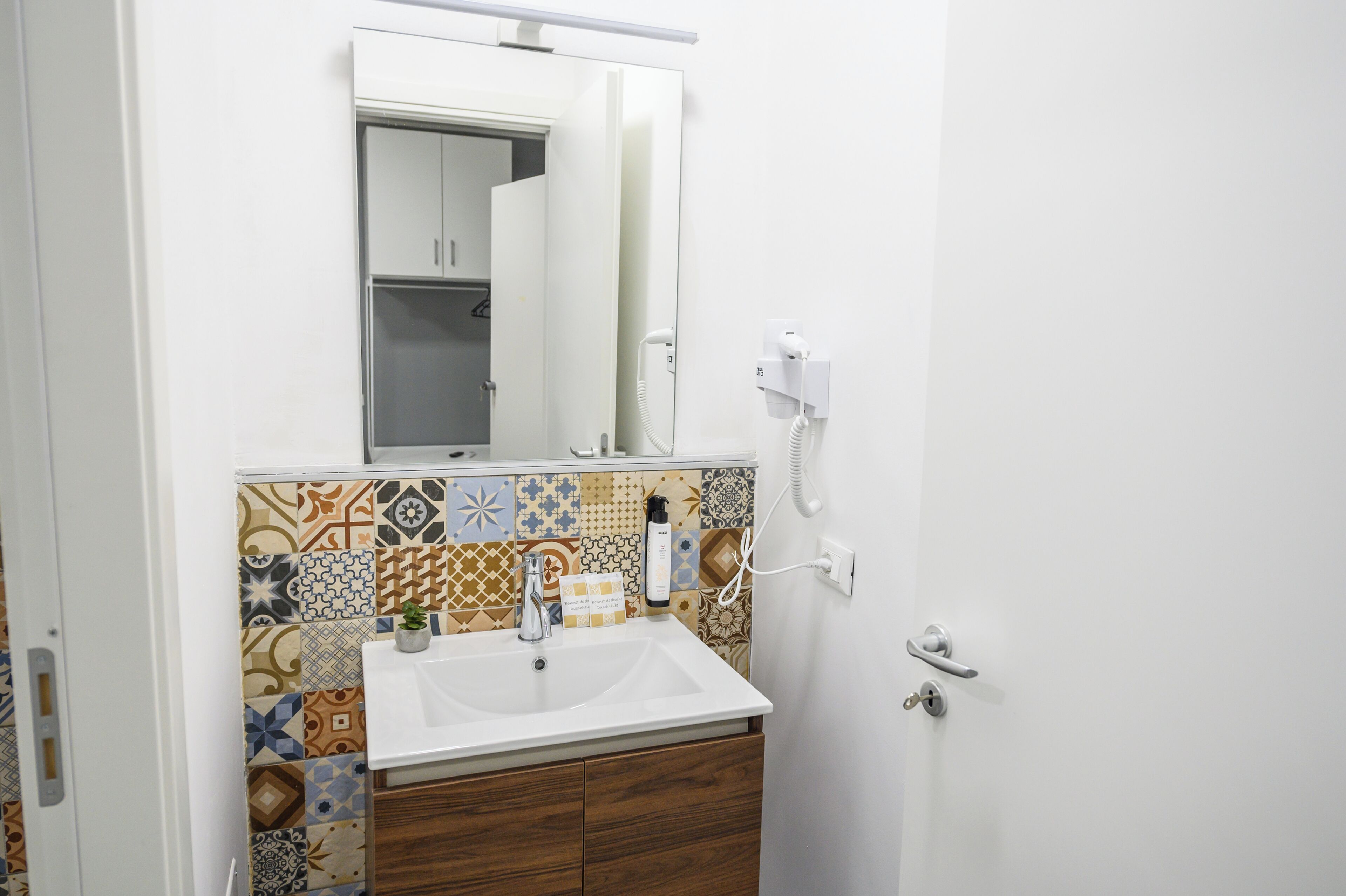 Un baño con un lavamanos blanco, un espejo encima y un salpicadero de azulejos estampados.