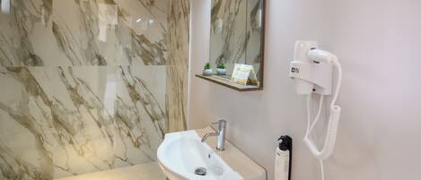 Un baño con pared de mármol, un lavabo, un espejo, un teléfono y una pequeña repisa con plantas.