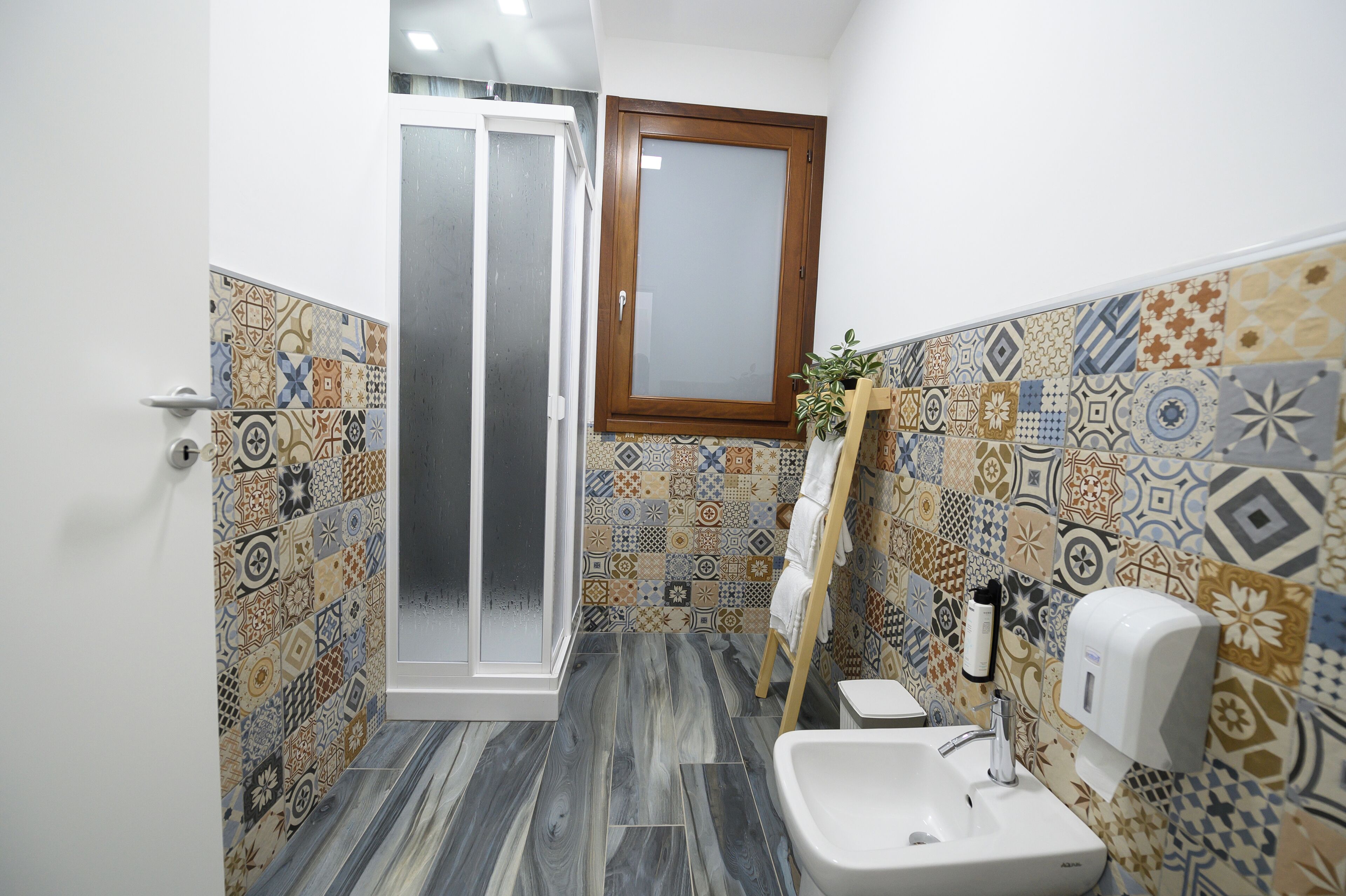 A bathroom with patterned tiles, a wooden cabinet, a towel rack, and a hand soap dispenser.