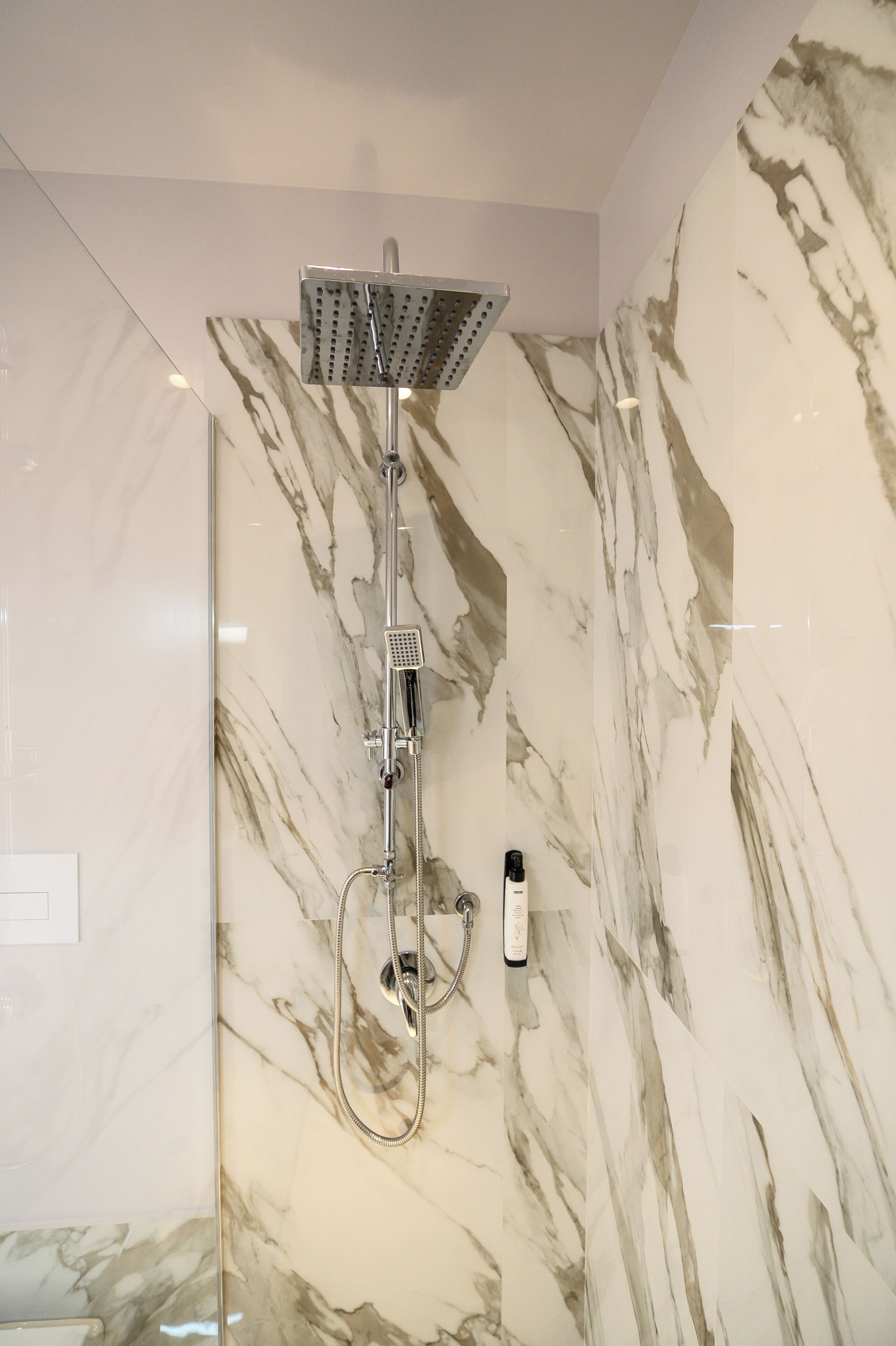 A shower with a handheld showerhead and a wall-mounted control panel.